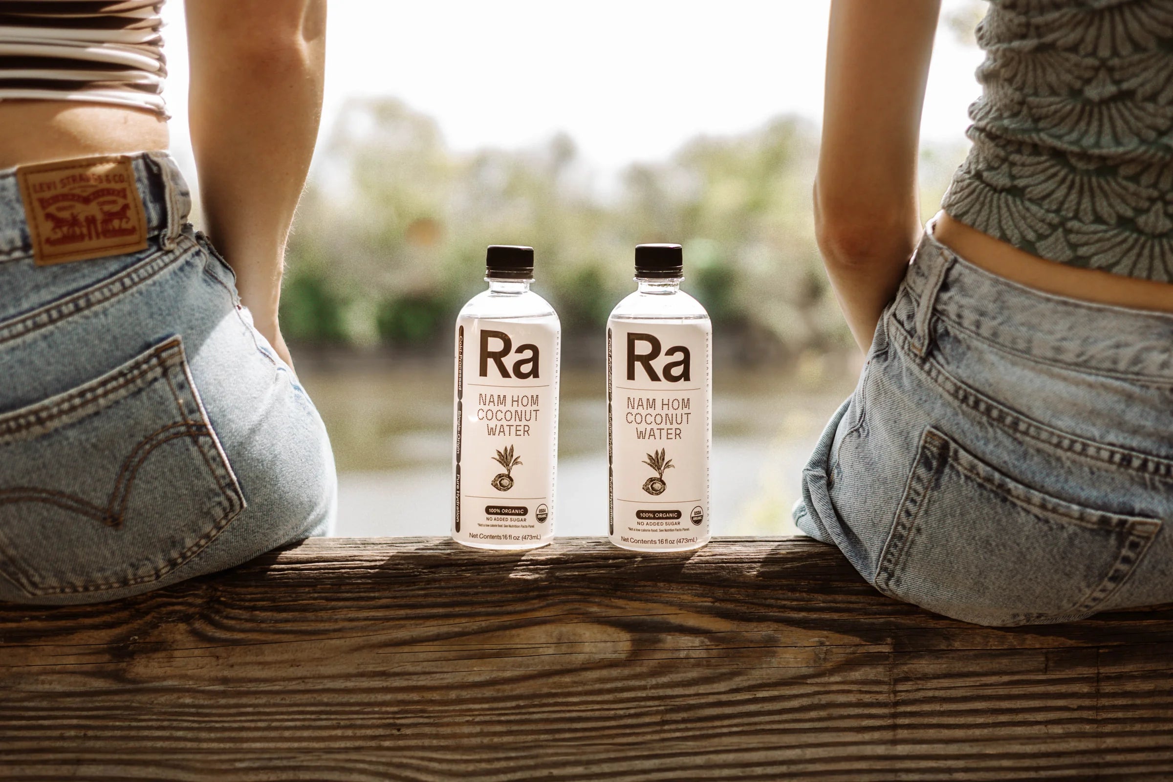 Two Ra coconut water bottles between friends on a bench